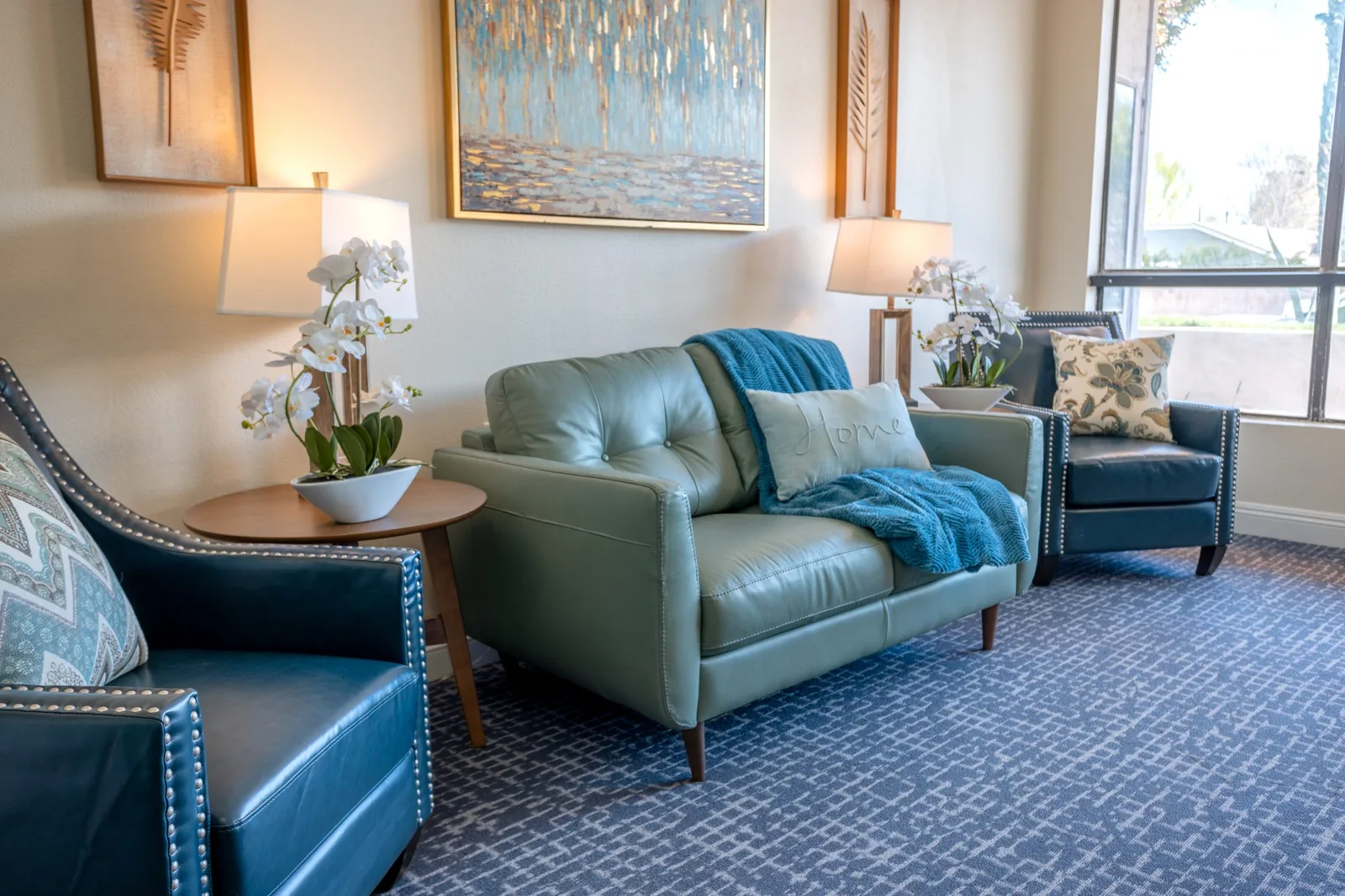 A bright lounge with teal armchairs and a sofa where residents gather